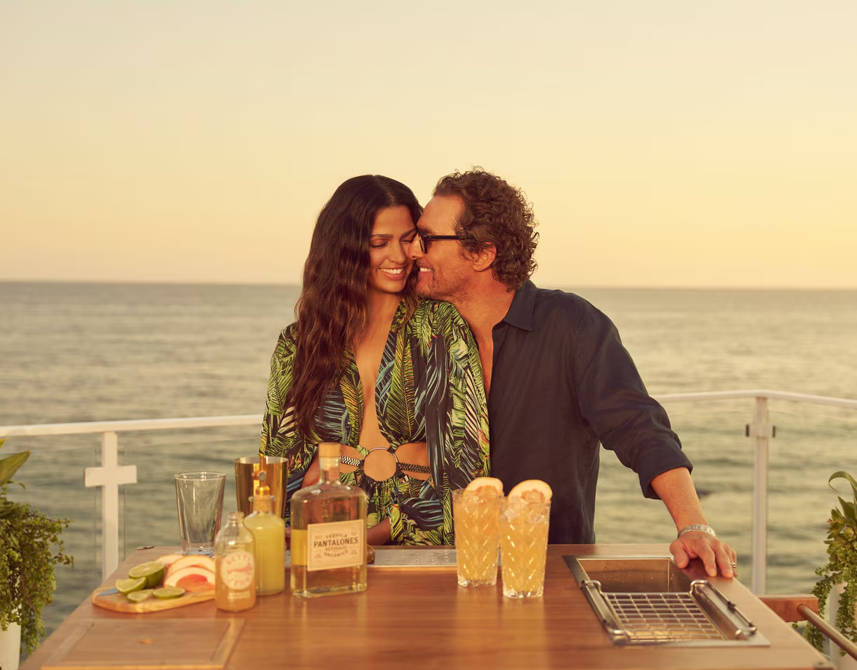 Matthew e Camila McConaughey no bar ao ar livre ao pôr do sol, junto a garrafas de Pantalones Organic Tequila.